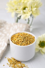 Photo of Fresh bee pollen granules and flowers on white tiled table, closeup