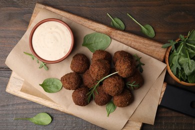 Photo of Delicious falafel balls, arugula, basil and sauce on wooden table, top view