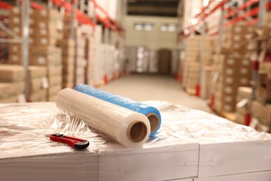 Photo of Rolls of different stretch wraps and utility knife on boxes in warehouse