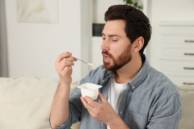 Photo of Handsome man eating delicious yogurt on sofa at home