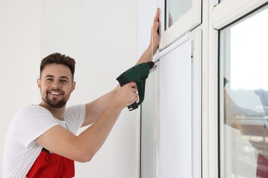 Photo of Worker in uniform installing roller window blind indoors