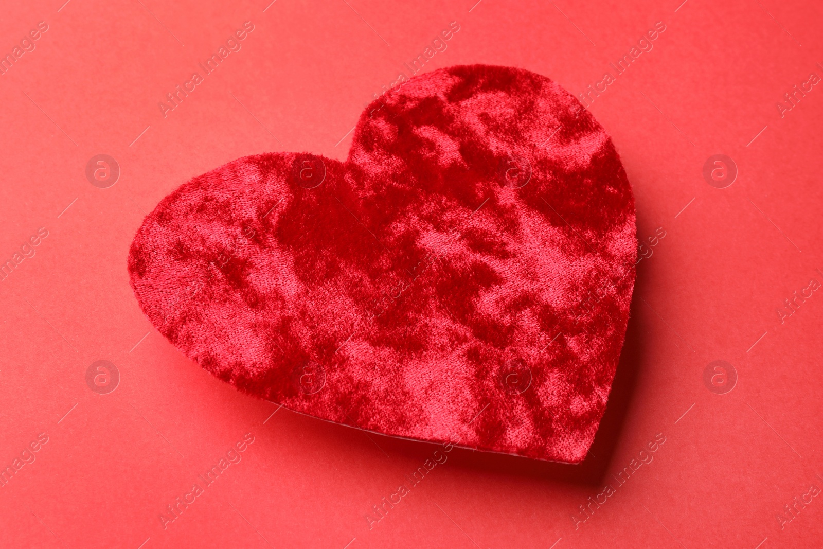 Photo of One velvet heart on red background, closeup