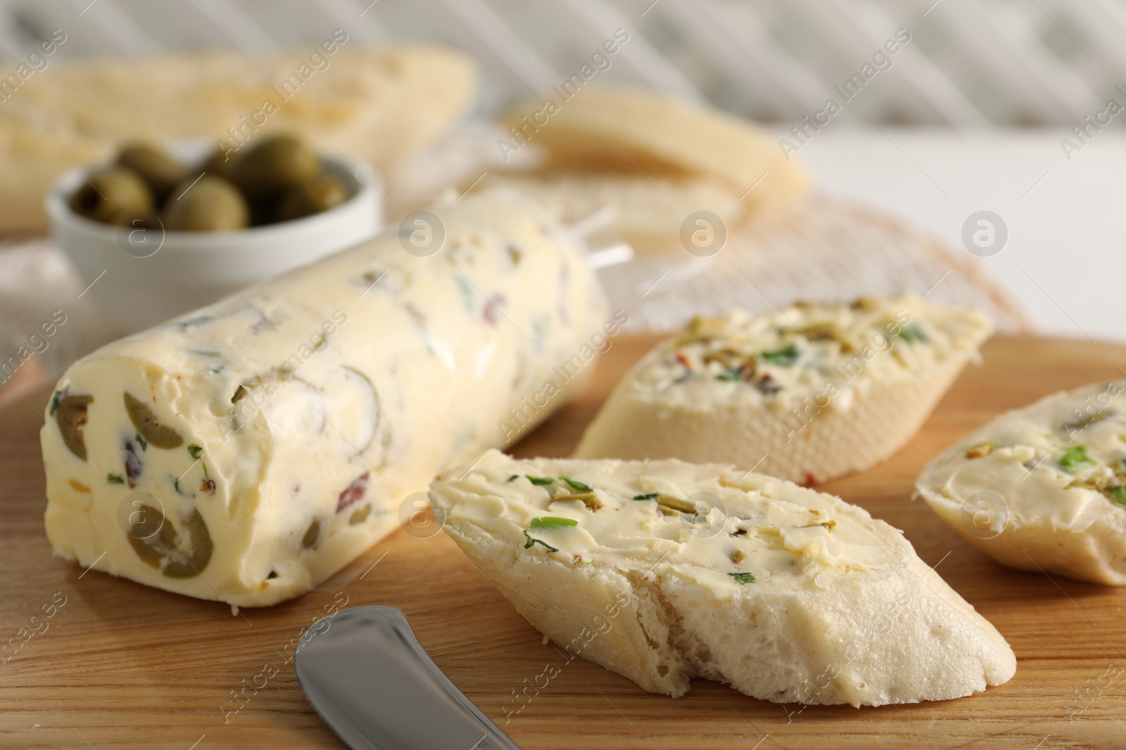 Photo of Tasty butter with olives, green onion and bread on wooden board, closeup