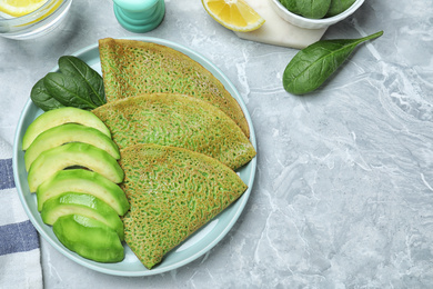 Delicious spinach crepes with avocado served on marble table, flat lay. Space for text