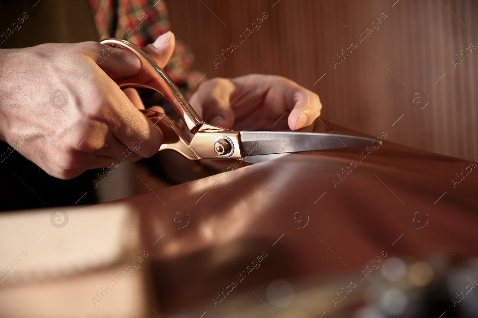 Photo of Man cutting leather with scissors in workshop, closeup