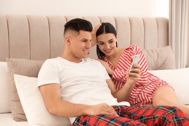 Happy couple in pyjamas using smartphone on bed at home