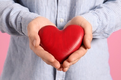 Man holding decorative heart on color background, closeup