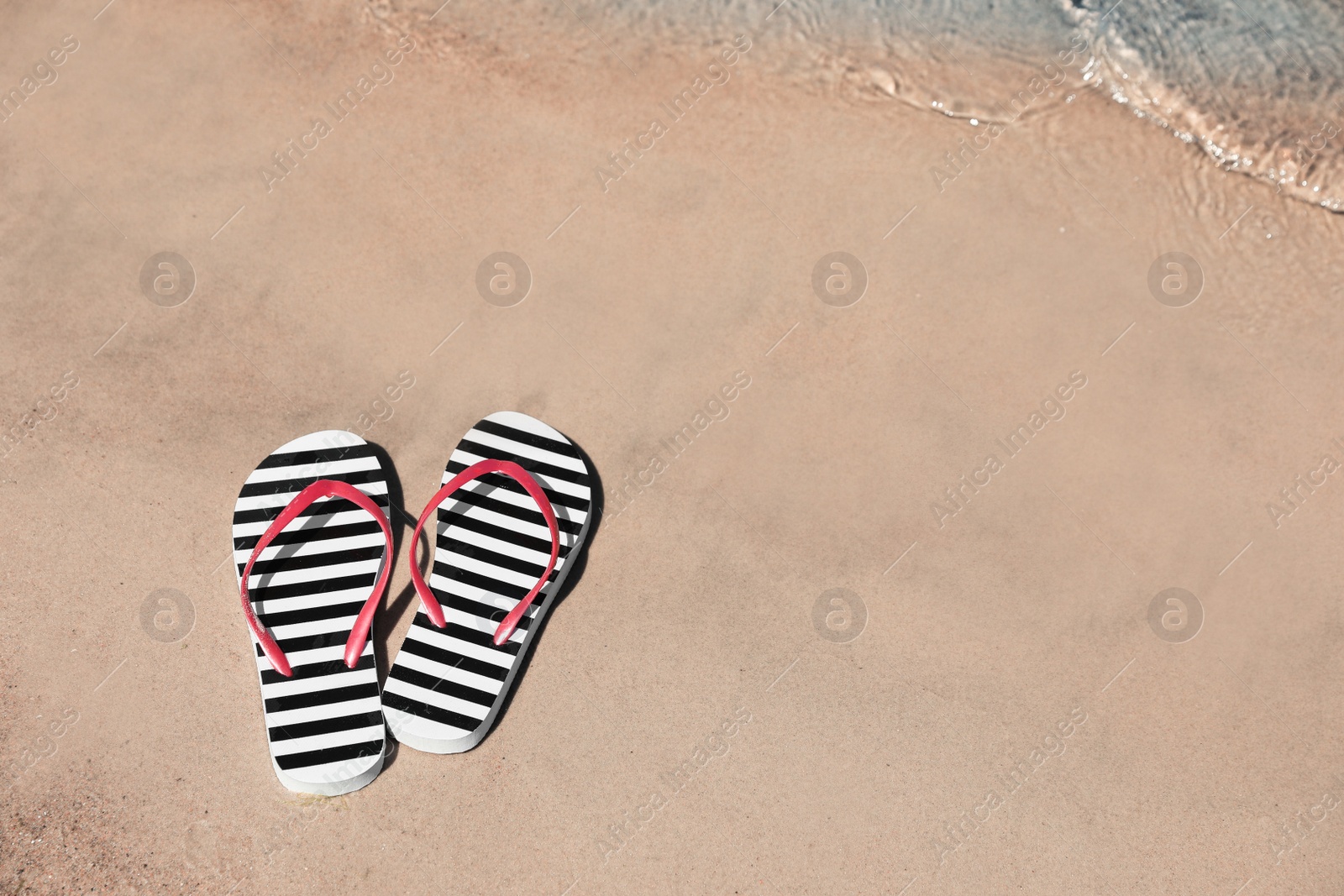 Photo of Stylish flip flops on sandy beach near sea, above view. Space for text