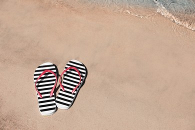 Stylish flip flops on sandy beach near sea, above view. Space for text