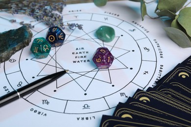 Photo of Zodiac wheel with sign triplicities, pen, tarot cards, gemstones and astrology dices on table, closeup