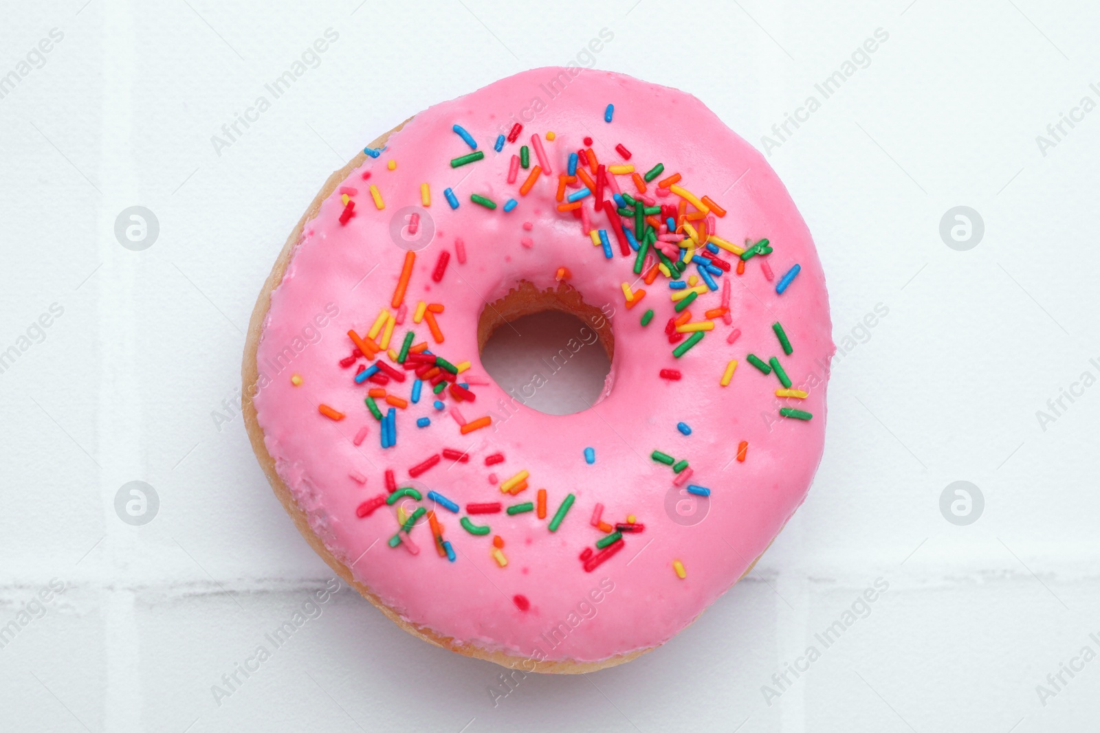 Photo of Tasty glazed donut decorated with colorful sprinkles on white table, closeup