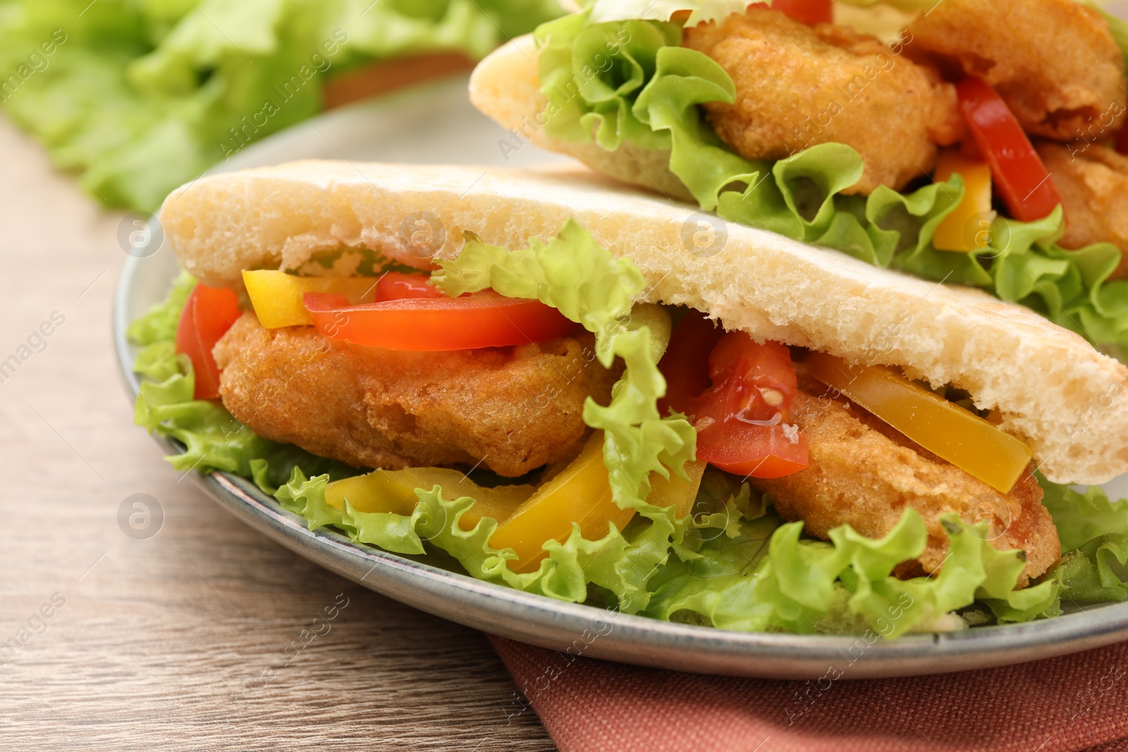 Photo of Delicious pita sandwiches with fried fish, pepper, tomatoes and lettuce on wooden table, closeup