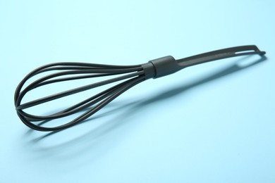 Photo of One whisk on light blue background, closeup