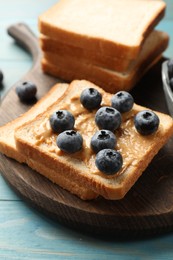 Photo of Delicious toasts with peanut butter and blueberries on light blue wooden table, closeup