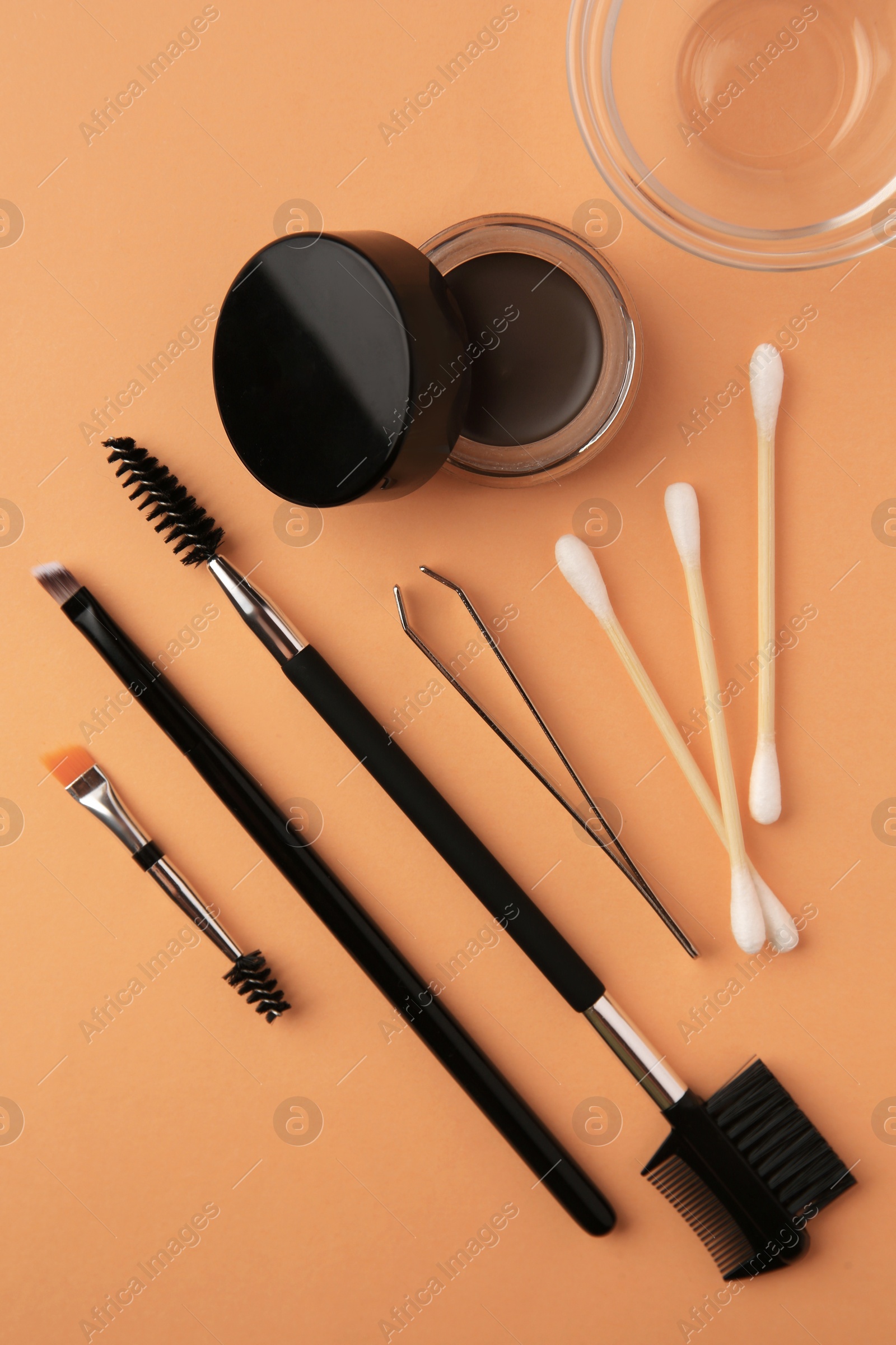 Photo of Eyebrow pomade with henna effect and professional tools on orange background, flat lay