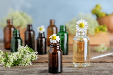 Photo of Bottles of essential oils with flowers on wooden table, space for text