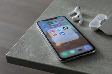 Photo of MYKOLAIV, UKRAINE - AUGUST 10, 2021: Apple iPhone X, AirPods and charging case on grey table. Screen with different social media icons