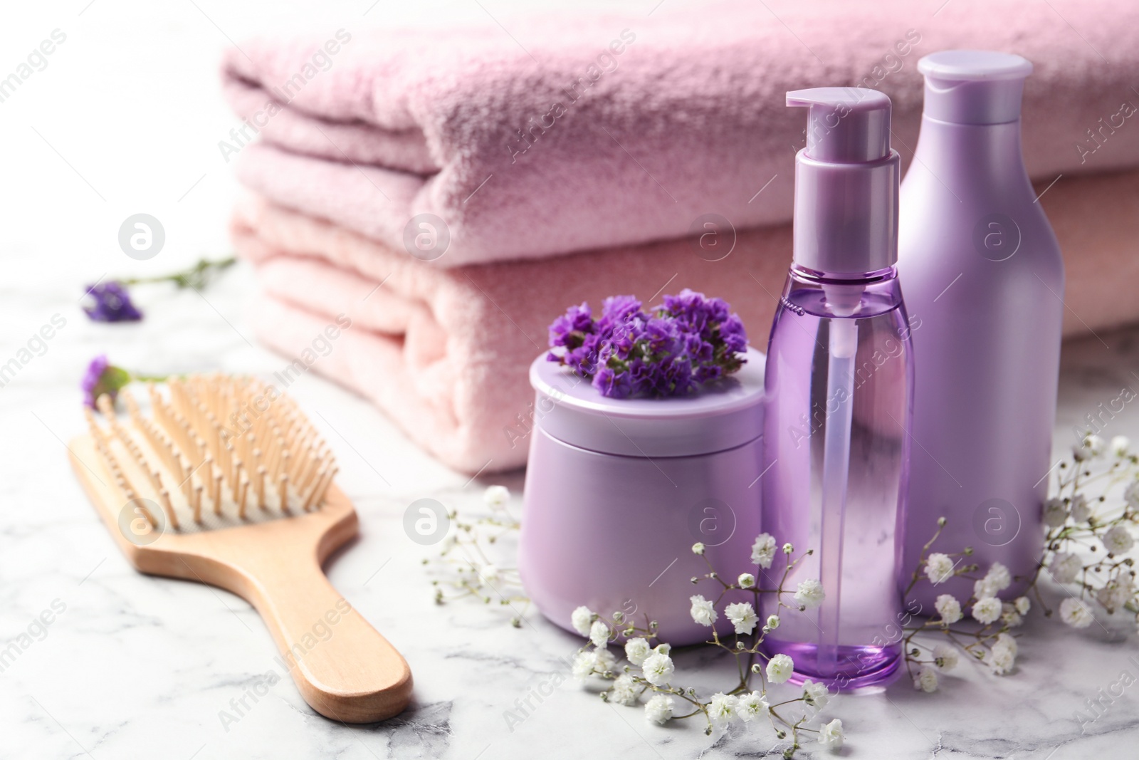 Photo of Set of hair cosmetic products, brush and flowers on  white marble table table