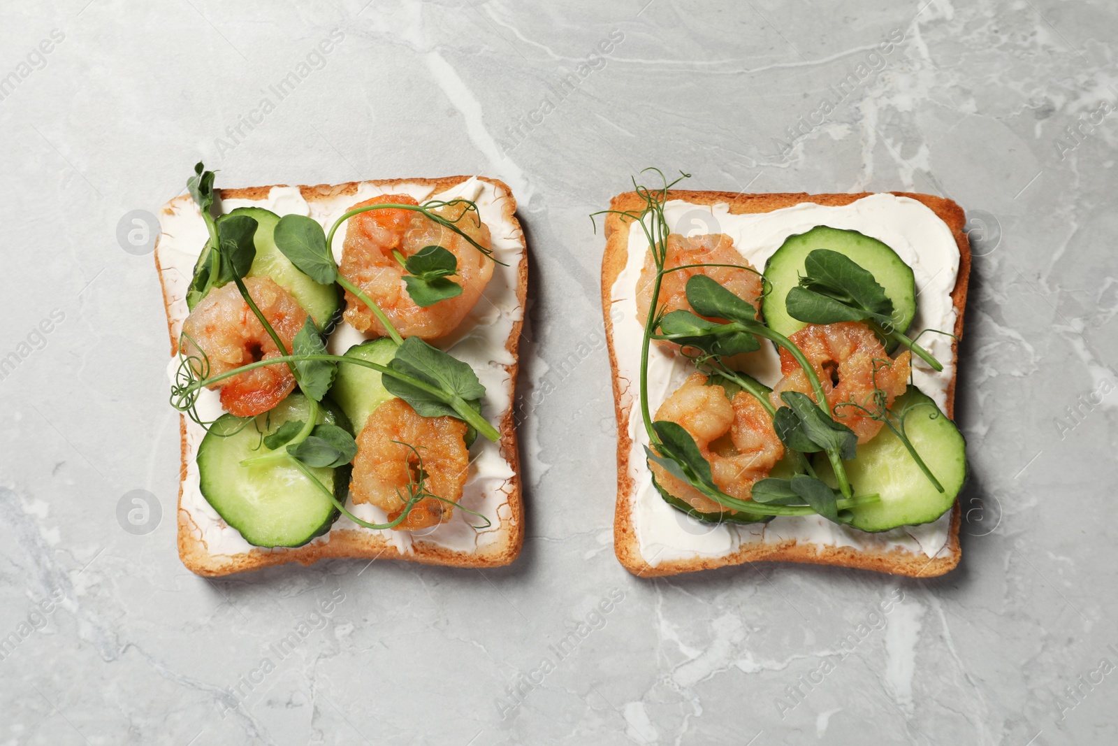 Photo of Tasty toasts with cream cheese, shrimps, cucumbers and microgreens on grey marble table, flat lay