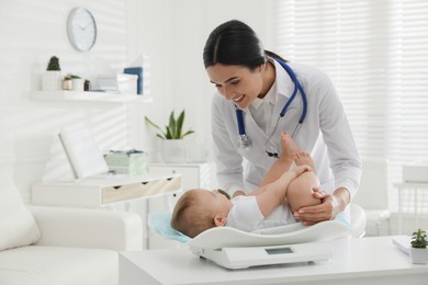 Photo of Young pediatrician weighting cute little baby in clinic