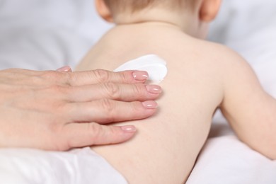 Woman applying body cream onto baby`s back on bed, closeup