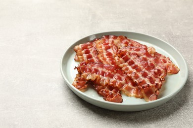 Plate with fried bacon slices on grey textured table, closeup. Space for text