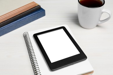 Photo of E-book reader with stationery and cup of tea on white wooden table. Space for text
