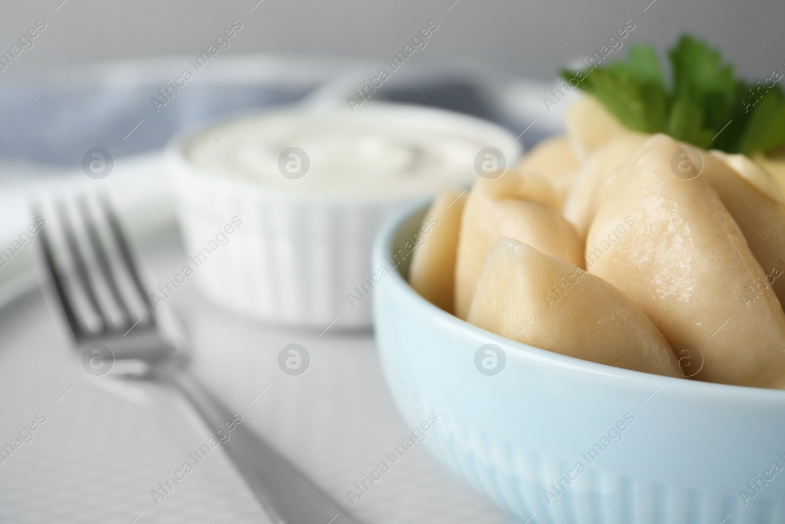 Photo of Delicious cooked dumplings and sour cream on table, closeup