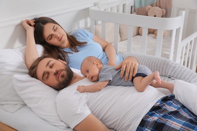 Photo of Tired young parents with their baby sleeping in bed at home