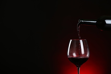 Pouring wine from bottle into glass on dark background, space for text