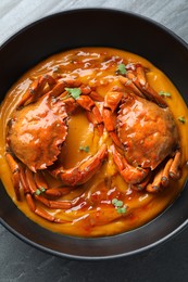 Delicious boiled crabs with sauce in bowl on grey table, top view