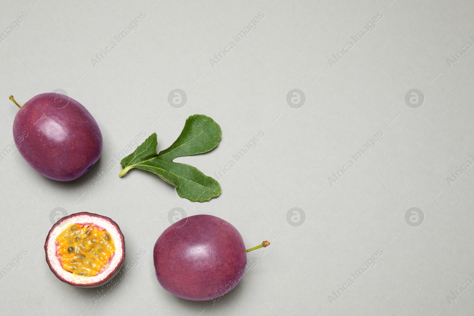 Photo of Fresh ripe passion fruits (maracuyas) with green leaf on grey background, flat lay. Space for text
