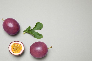 Fresh ripe passion fruits (maracuyas) with green leaf on grey background, flat lay. Space for text