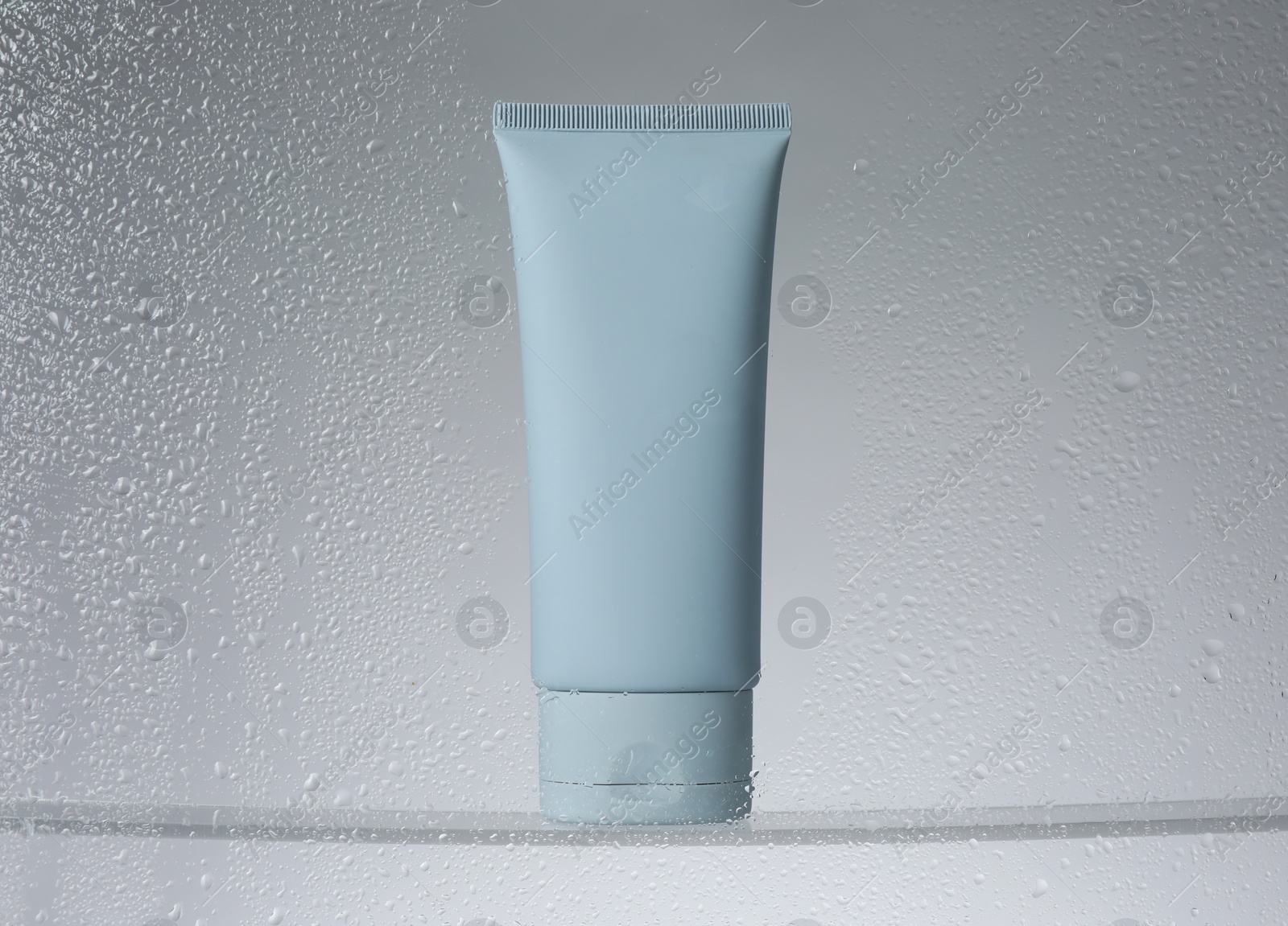 Photo of Tube with moisturizing cream on light background, view through wet glass