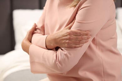 Mature woman suffering from pain in arms on bed, closeup. Rheumatism symptom