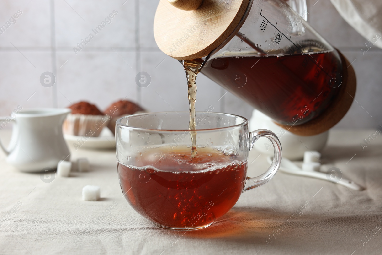 Photo of Pouring warm tea into cup on light table, closeup