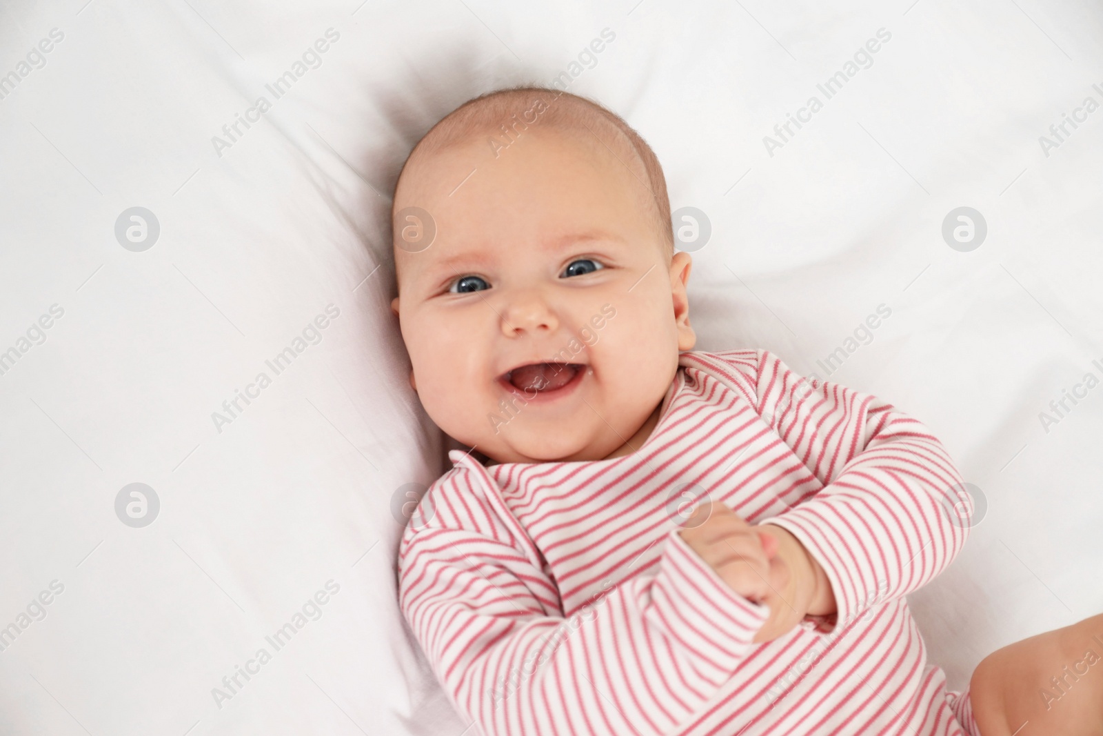 Photo of Cute little baby lying on white fabric, above view