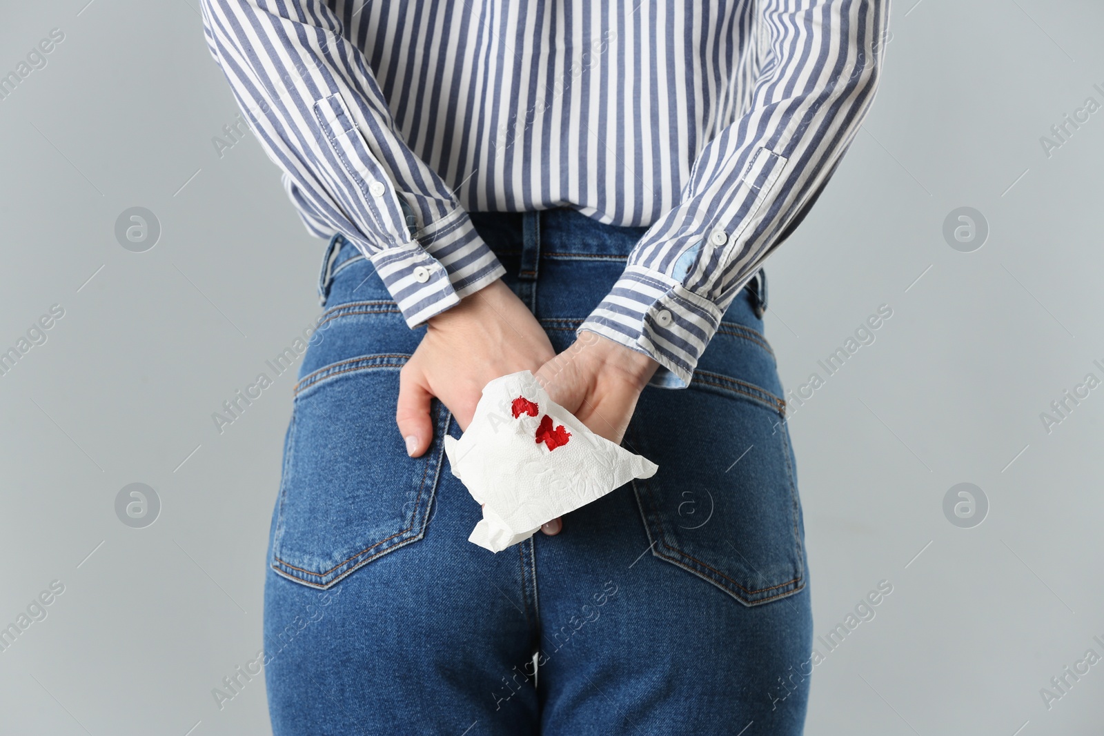 Photo of Woman holding toilet paper with blood stain on light grey background, closeup. Hemorrhoid concept