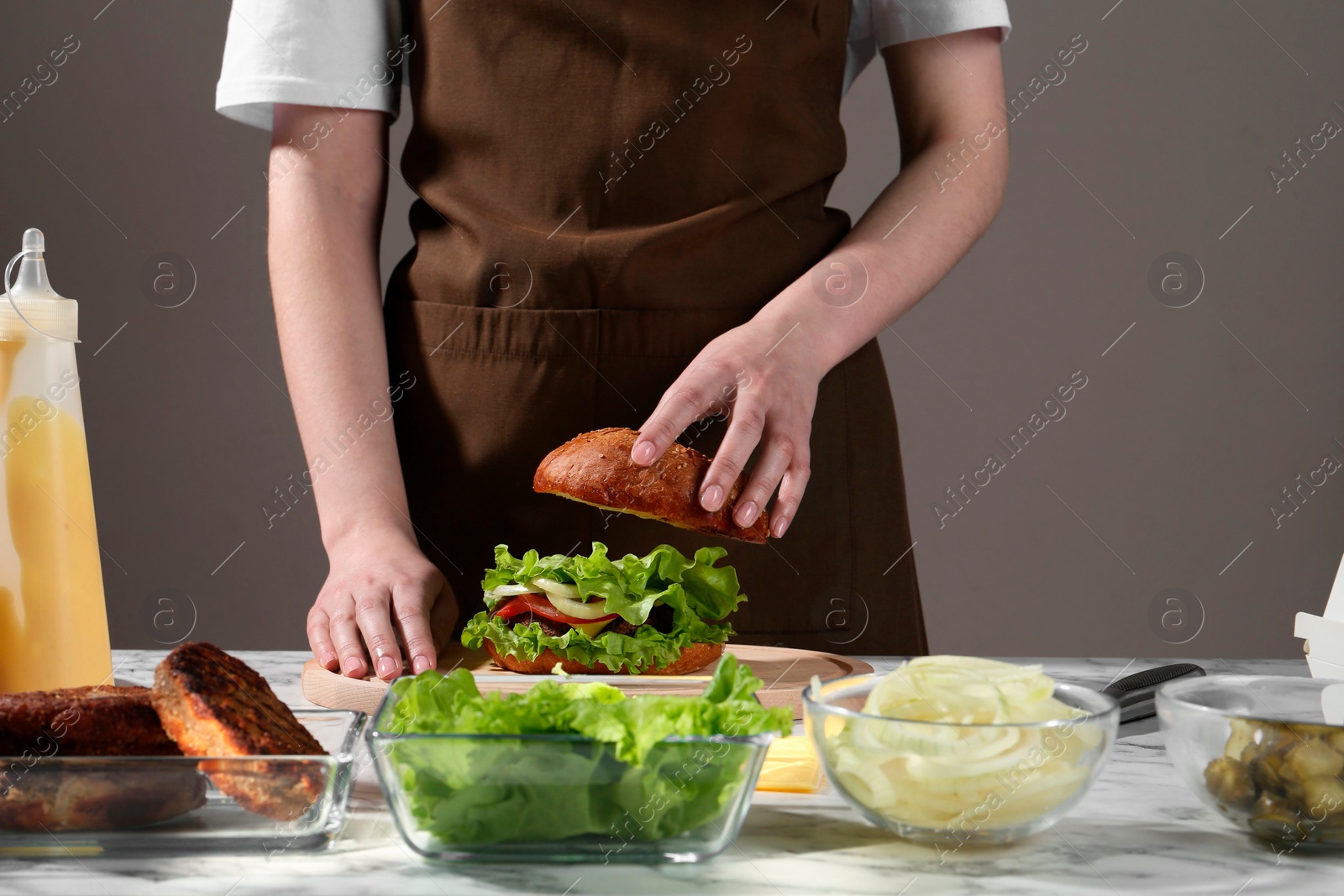 Photo of Woman making delicious vegetarian burger at white marble table, closeup