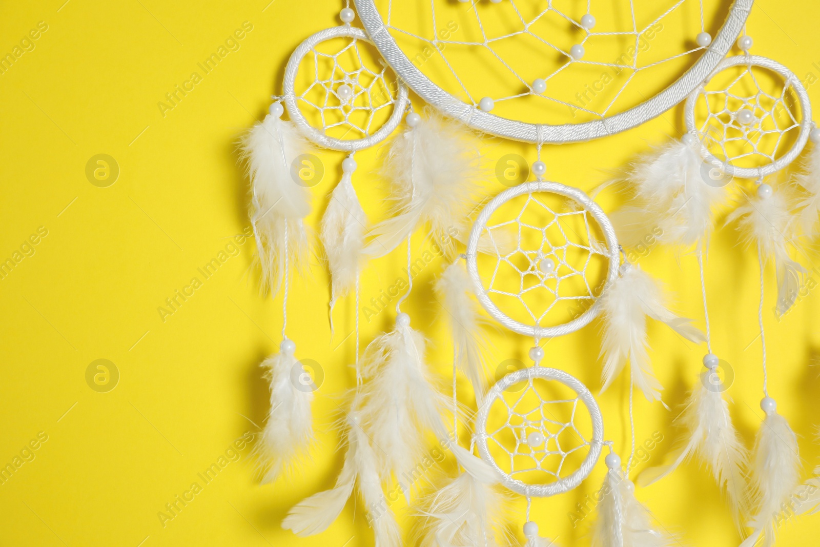 Photo of Beautiful dream catcher hanging on yellow background, closeup