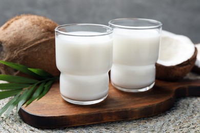 Glasses of delicious coconut milk, palm leaf and coconuts on table