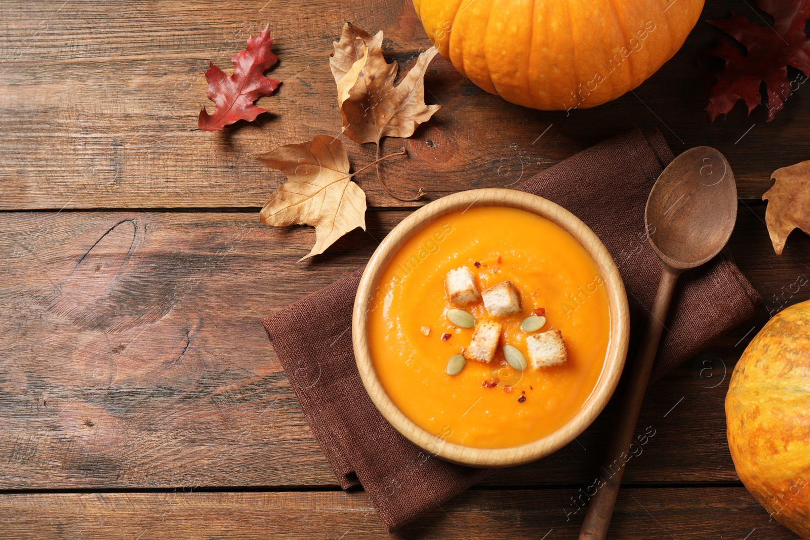 Photo of Bowl with tasty pumpkin cream soup on wooden table, flat lay. Space for text