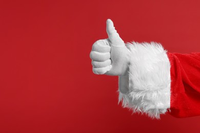 Photo of Merry Christmas. Santa Claus showing thumbs up on red background, closeup. Space for text