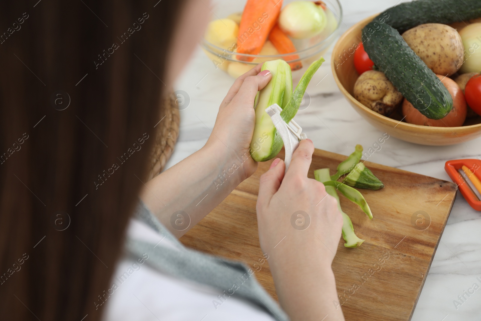 Photo of Woman peeling fresh zucchini at white marble table, closeup