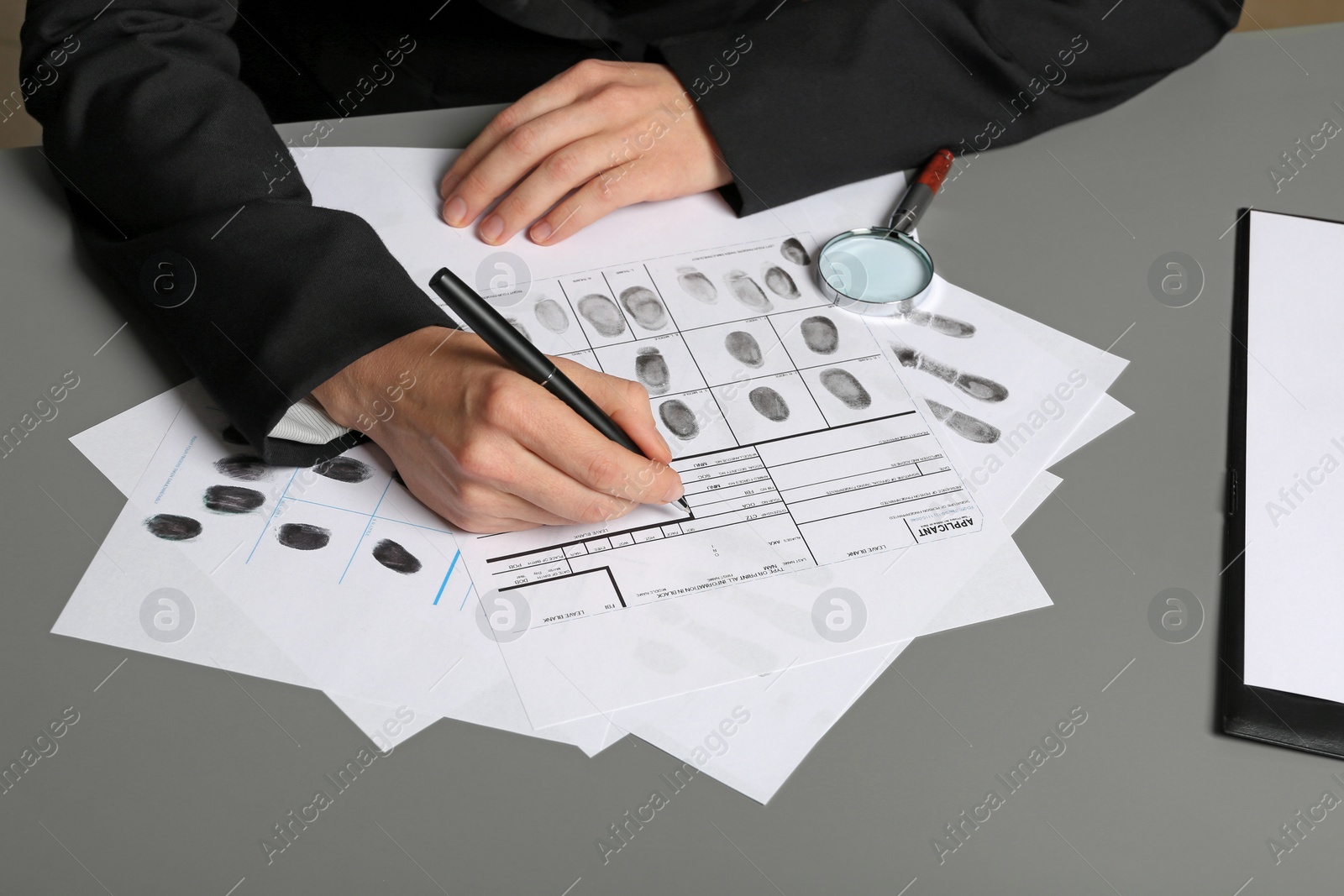 Photo of Female criminalist filling fingerprints card at table, closeup