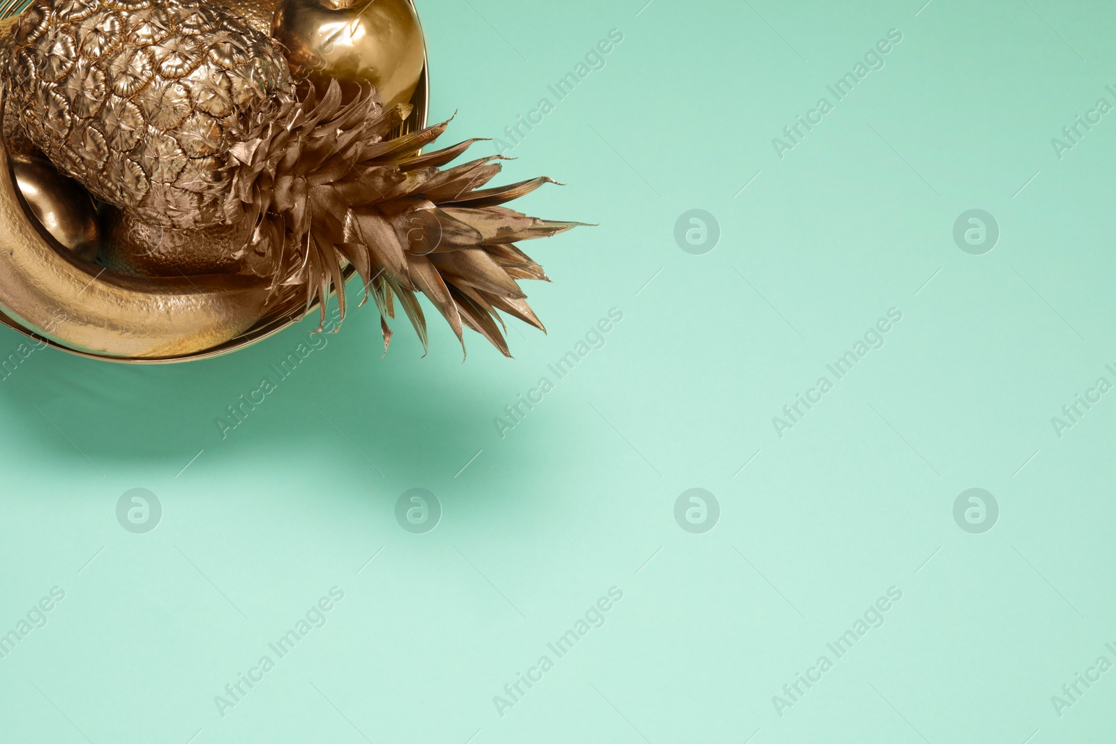 Photo of Golden bowl with fruits on turquoise background, top view. Space for text