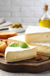 Photo of Tasty brie cheese with basil, bread and almonds on wooden board
