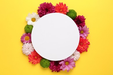 Frame made of beautiful chrysanthemum flowers and blank card on yellow background, flat lay. Space for text