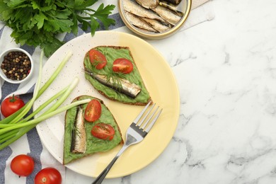 Photo of Delicious sandwiches with sprats, tomatoes, avocado puree and dill served on white marble table, flat lay. Space for text