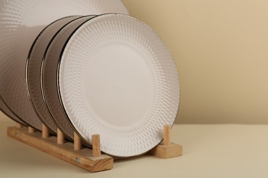 Drying rack with beige ceramic plates on pale yellow table, closeup. Space for text